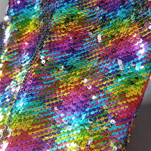 May include: Rainbow iridescent fabric with a scale-like pattern made of sequins. The sequins are arranged in rows and are a variety of colors, including red, orange, yellow, green, blue, indigo, and violet.