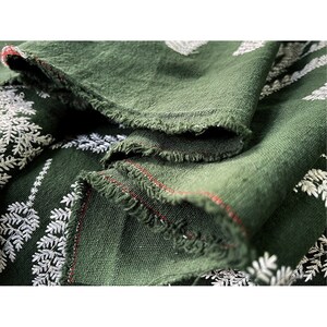 May include: Close-up of a dark green fabric with a white embroidered fern pattern. The fabric has a raw edge and is folded over itself.