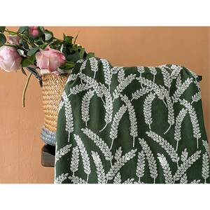 May include: Green fabric with a white floral pattern. The fabric features a repeating design of white sprigs on a dark green background.