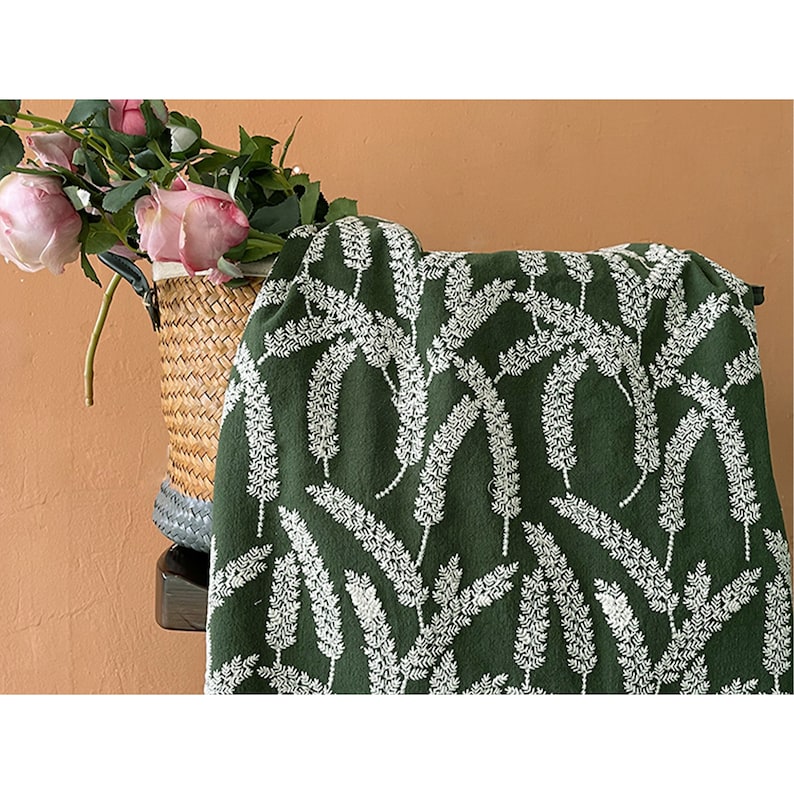 May include: Green fabric with a white floral pattern. The fabric features a repeating design of white sprigs on a dark green background.