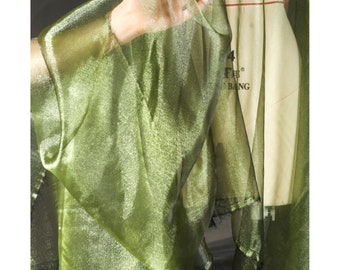 May include: A sheer, olive green fabric is draped, with light reflecting off its surface. The fabric appears to be a lightweight material, possibly silk or a similar textile. The fabric is held up, revealing its texture and color.
