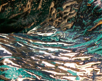 May include: Close-up of a green and gold fabric with a textured, wavy pattern. The fabric has a metallic sheen and is likely used for upholstery or clothing.