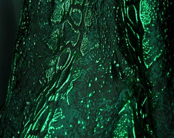 May include: Close-up of a dark green fabric with a textured, embossed pattern. The fabric has a subtle sheen and a slightly wrinkled appearance.