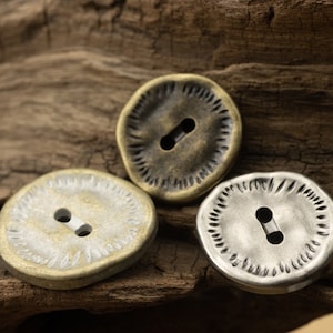 Könnte beinhalten: Drei Metallknöpfe mit einem dekorativen Design. Die Knöpfe sind rund und haben ein einzelnes Loch in der Mitte. Die Knöpfe sind in verschiedenen Gold- und Silbertönen.