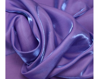 May include: Close-up of a soft, iridescent purple fabric with a subtle sheen. The fabric is smooth and flowing, creating a luxurious look.