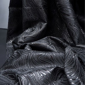 May include: Black fabric with a silver metallic swirl pattern. The fabric has a textured, woven look.