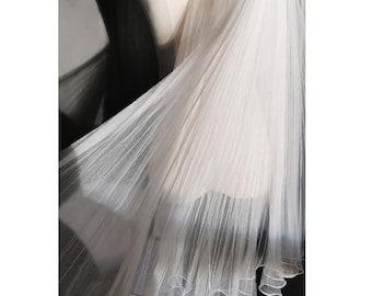May include: A white tulle veil with a pleated design. The veil is draped over a mannequin and has a scalloped edge.