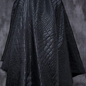 Könnte beinhalten: Schwarzer Stoff mit einem strukturierten Krokodilhautmuster. Das Material ist drapiert und zeigt Falten und Schatten. Der Stoff hat eine matte Oberfläche und eine dunkle, neutrale Farbe.
