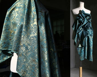 May include: A teal and gold fabric with a textured, metallic finish. The fabric is draped over a mannequin and is shown in two different styles.