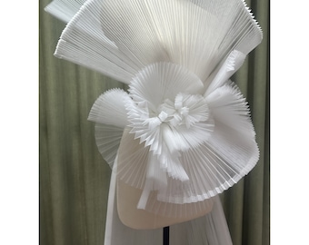 May include: White pleated fabric arranged in a large, abstract flower shape. The fabric is delicate and translucent, creating a soft and ethereal look.