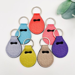 May include: Seven teardrop shaped keychains with different colored fabric and white polka dots. The keychains are made of fabric and have a black stitched border. The keychains have a silver metal ring. The colors of the keychains are purple, blue, gray, green, brown, pink, and red.
