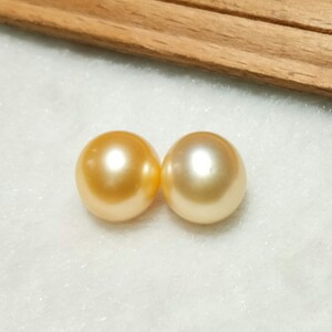 Puede incluir: Dos perlas redondas de tono dorado con una superficie lisa y brillante. Cada perla presenta un brillo reflectante y un color amarillo met&aacute;lico c&aacute;lido, mostrando una forma esf&eacute;rica y un acabado pulido que captura la luz de manera uniforme.