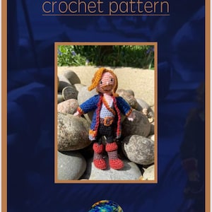 Può includere: Un modello all'uncinetto intitolato "Guybrush Threepwood" è visualizzato su uno sfondo blu. Il modello include una piccola bambola all'uncinetto fatta a mano di un personaggio con capelli rossi, una giacca blu e stivali rossi. La bambola è appoggiata su un letto di rocce. Il logo Gin Makes si trova nell'angolo in basso.