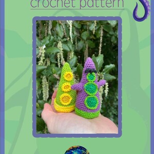 Puede incluir: Dos figuras de tentáculos de ganchillo hechas a mano. Una es verde y amarilla, la otra es morada y verde. Las figuras tienen detalles circulares y se sostienen en una mano. La imagen incluye el texto "Purple and Green Tentacle crochet pattern."