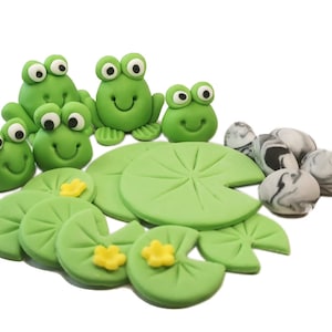 Könnte beinhalten: Grüne Fondant-Frösche und Seerosen mit schwarz-weiß marmorierten Fondant-Steinen. Dies sind Tortendekorationen für eine Frosch-Mottoparty.