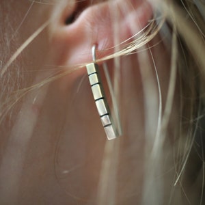 以下が含まれることがあります： テクスチャ加工された表面を持つシルバーバーのイヤリング。イヤリングは人の耳からぶら下がっています。