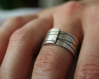May include: A silver ring with a textured design. The ring is made of multiple bands with a wavy pattern.