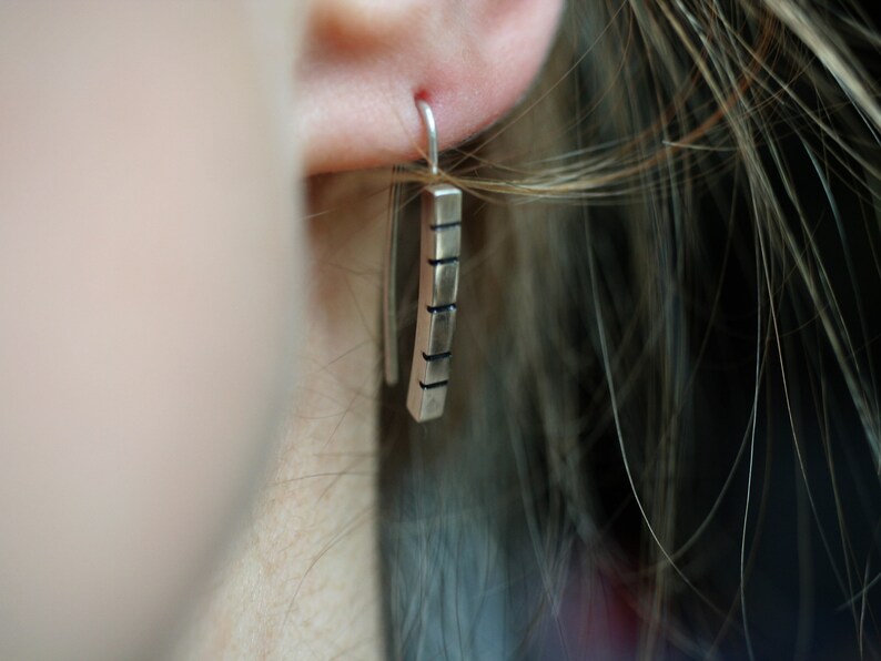 以下が含まれることがあります： 長方形でテクスチャ加工された表面を持つシルバーのドロップイヤリング