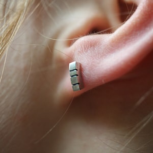 以下が含まれることがあります： 複数の正方形が積み重ねられた長方形のデザインのシルバー製のイヤリング