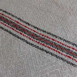 Könnte beinhalten: Nahaufnahme eines weißen Leinenstoffes mit einem gewebten Streifenmuster in Rot und Grau.