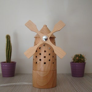 May include: A wooden windmill-shaped diffuser with a light wood finish and a silver metal accent. The diffuser is sitting on a table with two potted cacti.