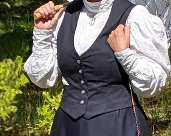 Puede incluir: Una mujer con un atuendo vintage, que incluye un chaleco negro, una falda larga y una blusa blanca con detalles de encaje. Lleva un sombrero con una cinta azul y sostiene un parasol. Un pequeño bolso con bordado floral azul cuelga de su lado.