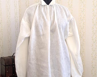 Può includere: Una camicia bianca di lino con scollo arricciato e maniche lunghe. La camicia è su un manichino e ha un design semplice e classico.