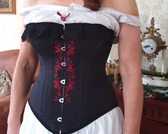 May include: A black corset with red floral embroidery and silver buttons. The corset is worn over a white petticoat.