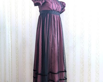 May include: A vintage-style formal dress in a deep burgundy color, featuring a black overlay with small polka dots. The dress has short, puffed sleeves, a black waist sash, and a floor-length skirt with lace trim. The dress is displayed on a mannequin.