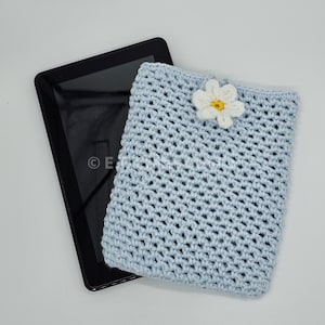 May include: A light blue crocheted tablet case with a white flower accent. The case is made with a simple stitch pattern and has a subtle texture.