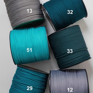 May include: Spools of cord in various colors, including gray, teal, and dark green. Each spool has a number printed on it, such as "13" or "32". The cords are tightly wound, and the spools are arranged in a visually appealing pattern.