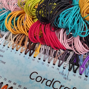 May include: A color sample card labeled CordCraft featuring numerous loops of elastic cord in various shades including pink, yellow, black, turquoise, red, and brown. The card includes numbered slots and text labels for gold, silver, and reflective cord types.