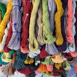 May include: A collection of numerous bundles of elastic cord in a wide variety of colors including yellow, red, green, blue, purple, orange, and neutral tones. Each bundle is neatly coiled and secured with small pieces of matching string.