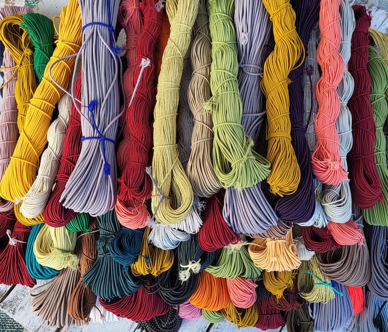 May include: A collection of numerous bundles of elastic cord in a wide variety of colors including yellow, red, green, blue, purple, orange, and neutral tones. Each bundle is neatly coiled and secured with small pieces of matching string.