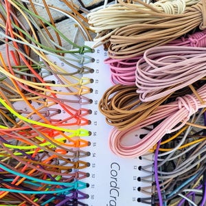 May include: A color sample card labeled CordCraft with numbered slots holding various lengths of thin, flexible elastic cord in a wide spectrum of colors including neon yellow, orange, pink, brown, beige, green, blue, and purple.