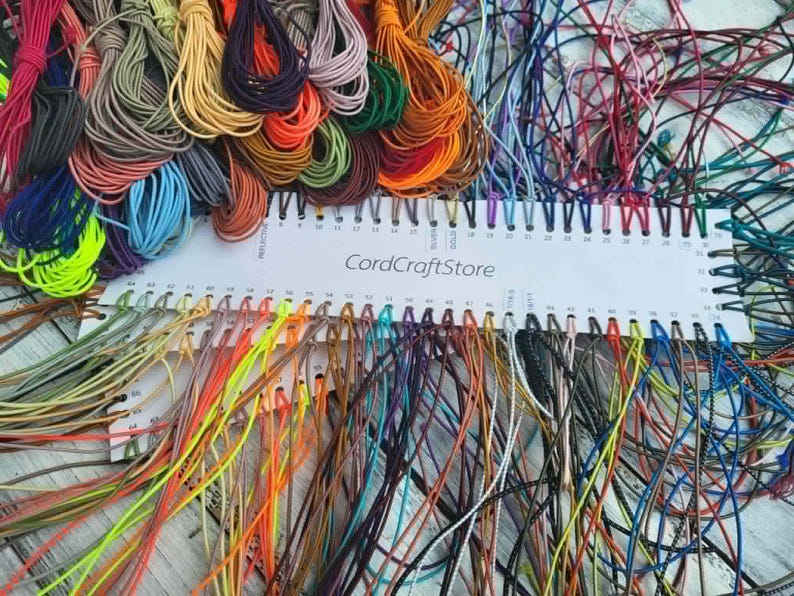 May include: A white plastic color chart labeled CordCraftStore featuring numerous numbered slots. Each slot holds a thin, multi-colored cord in various shades including neon yellow, blue, orange, red, purple, green, brown, and black.