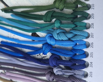 May include: A color swatch card featuring numbered rows from 200 to 213, each displaying a braided cord tied in a knot. The cords transition through a spectrum of colors including red, tan, lavender, purple, blue, teal, green, and light brown.