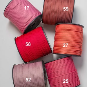 Könnte beinhalten: Sechs Garnrollen in verschiedenen Rosa-, Rot- und Orangetönen, jeweils mit einer weißen Nummer versehen: 17, 59, 58, 27, 52 und 25. Die Schnüre sind fest auf schwarze Kunststoffspulen gewickelt und weisen eine glatte, gleichmäßige Textur auf.