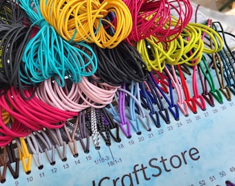 May include: A color sample card labeled CraftStore featuring numerous loops of elastic cord in various shades including yellow, turquoise, black, pink, red, blue, and purple, organized by numbered slots ranging from 9 to 52.