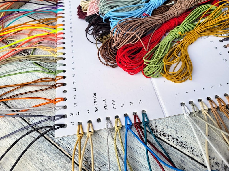 May include: A white display card with numbered holes and printed labels including REFLECTIVE, SILVER, and GOLD, featuring an assortment of colorful elastic cords looped through the holes. The cords come in various shades like red, yellow, green, blue, brown, and black.