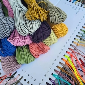 May include: A collection of colorful cords and threads, including pink, blue, green, and yellow, are displayed next to a color chart. The cords are bundled and arranged in a visually appealing manner, showcasing a variety of hues and textures.