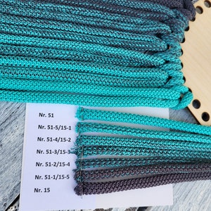 May include: A close-up of a white card with black text listing different sizes of teal and grey yarn. The yarn is arranged in rows on the card, with the largest size at the top and the smallest size at the bottom.