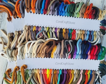 May include: A collection of multi-colored braided cords organized on white display cards labeled CordCraftStore. The cords feature a wide variety of solid colors, including red, blue, green, yellow, orange, brown, black, white, and grey.