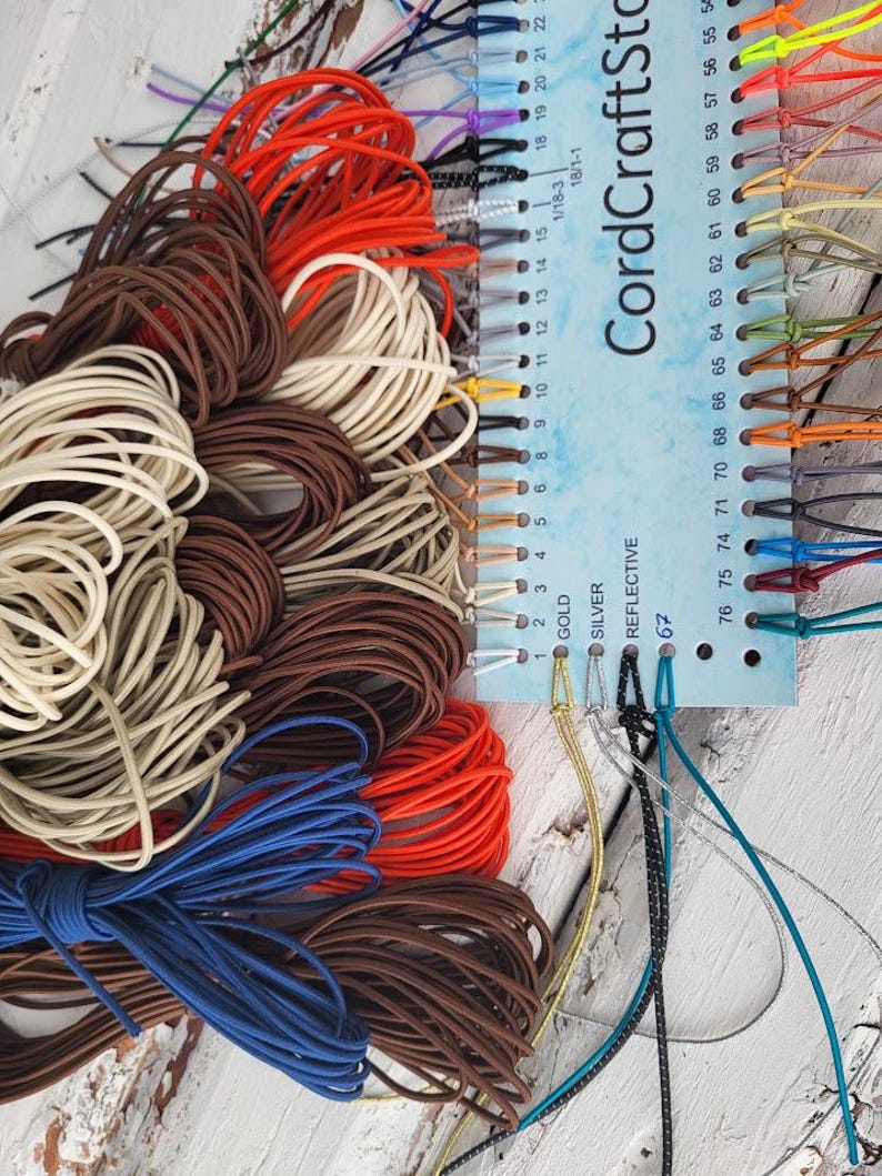 May include: A color sample card labeled CordCraftStore with numbered holes from 1 to 76, featuring various elastic cords in shades of red, brown, cream, blue, gold, silver, and reflective black, organized by color and attached to the card.