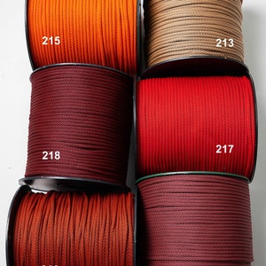 Op de afbeelding: Zes spoelen met gevlochten koord in diverse kleuren, waaronder oranje, beige, donkerrood, felrood en roestbruin, elk gelabeld met de nummers 215, 213, 218, 217, 216 en 226, gerangschikt in een raster voor verschillende knutselprojecten.