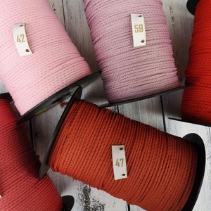 May include: Five spools of cotton cord in various colors, including pink, red, and orange. Each spool has a small leather tag with a number printed on it. The numbers are 42, 58, 40, 58, and 47.