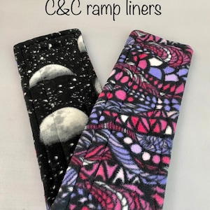 May include: Two C&C ramp liners. One is black with a white moon phase design. The other is black with a pink, purple, and white geometric pattern. The liners are made of a soft, quilted fabric.