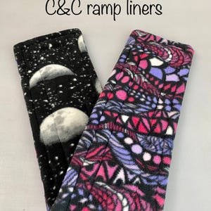 May include: Two rectangular C&C ramp liners with stitched edges. The left liner features a black background with white moon phases and stars. The right liner displays a vibrant geometric pattern in shades of pink, purple, black, and white.