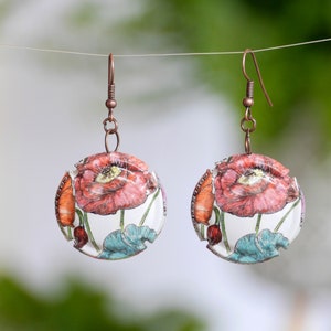 Peut inclure: Boucles d'oreilles rondes avec un motif floral de coquelicots rouges, des touches d'orange et des feuilles turquoise sur fond blanc. Les boucles ont des crochets cuivrés et sont suspendues à un fil fin, sur le thème botanique.