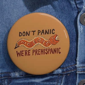May include: A brown button with a red and orange snake design and the text "Don't Panic We're Prehispanic".